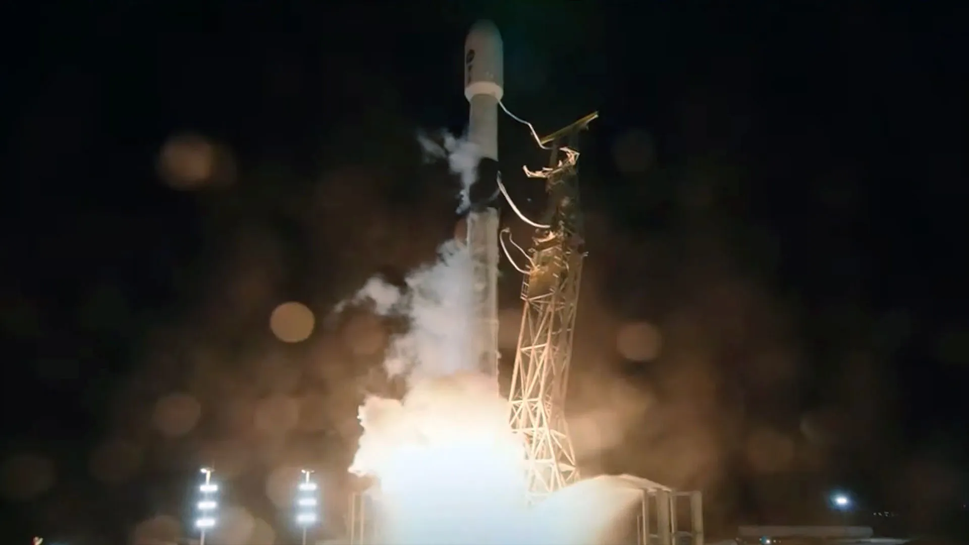 eine schwarz-weiße Rakete hebt von ihrer Startrampe mit einem hellen weißen Schub in den dunklen Nachthimmel ab.